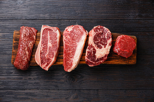 five cuts of red meat on a board against a black wood background